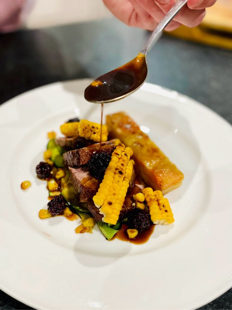 chef drizzling gravy over meat and sweetcorn main